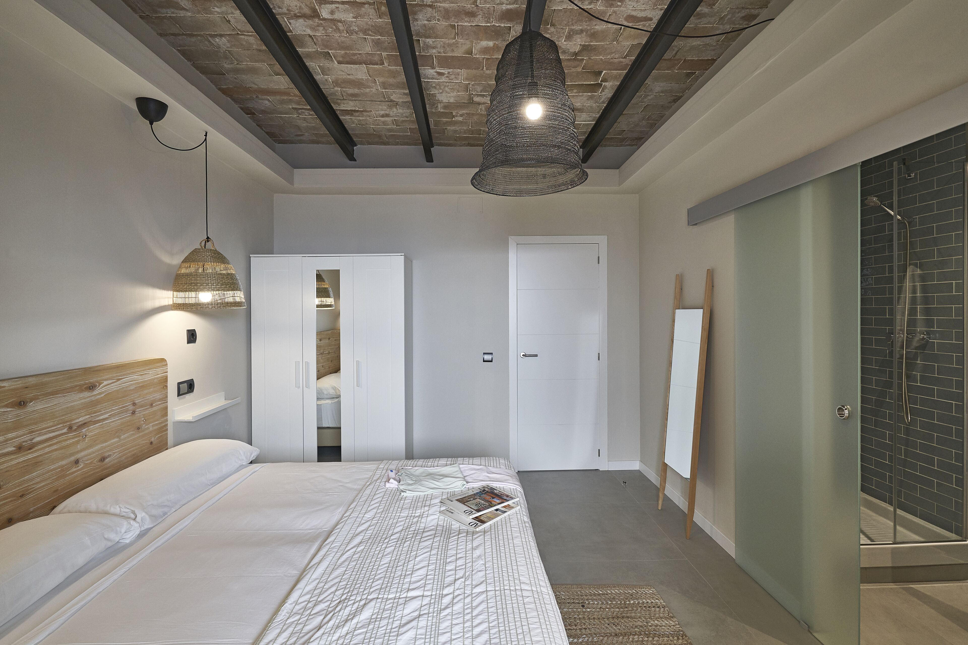 Een moderne slaapkamer met een houten hoofdbord, een bed met een beddengoed met patroon, een hanglamp, een inloopkast met schuifdeuren, en een douchecel met een glazen deur.