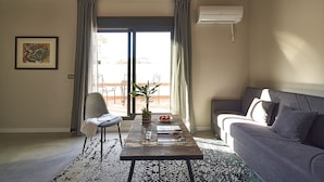 Una sala de estar con un sofá, una mesa de centro con una planta y un cuenco, una silla y un ventanal con cortinas.