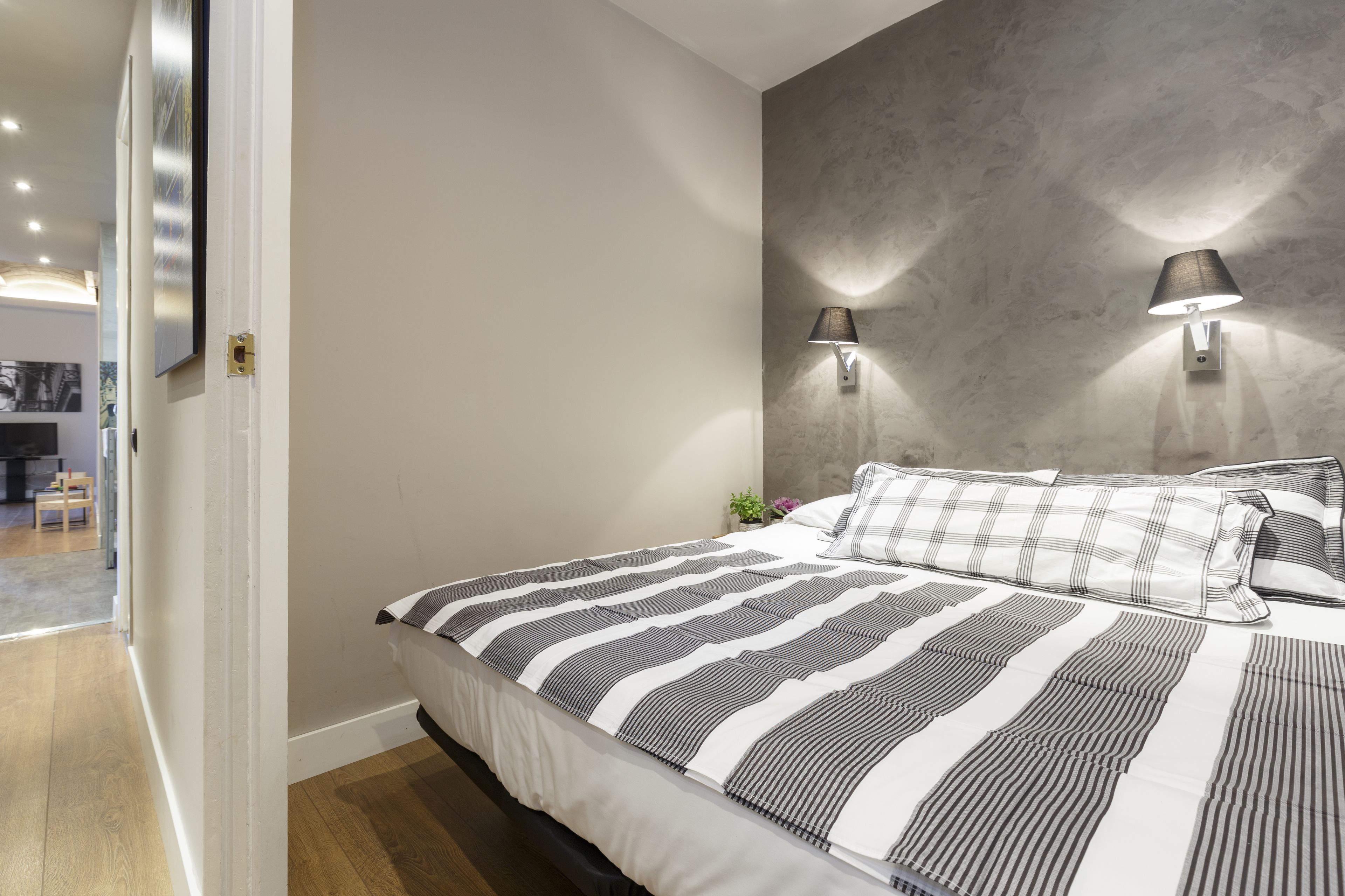 A bedroom with a large bed, two wall-mounted lamps, and a grey textured wall.