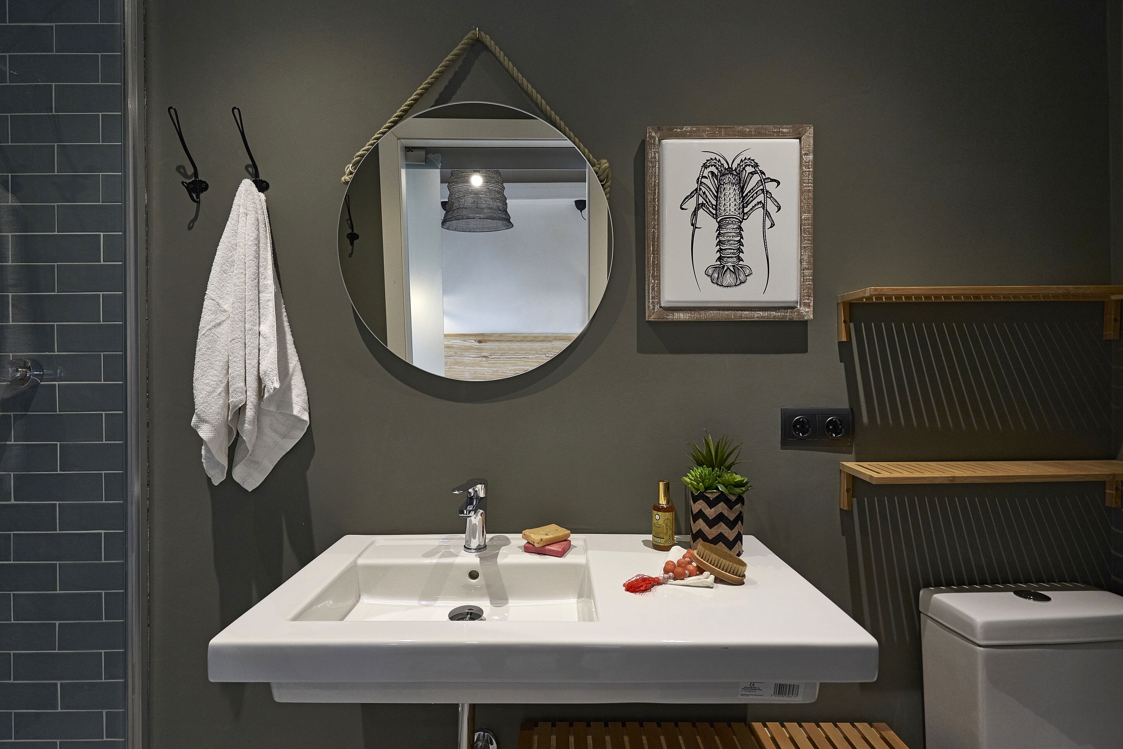 Un baño con un lavamanos blanco, un espejo, una obra de arte enmarco y una toalla colgada de un gancho.