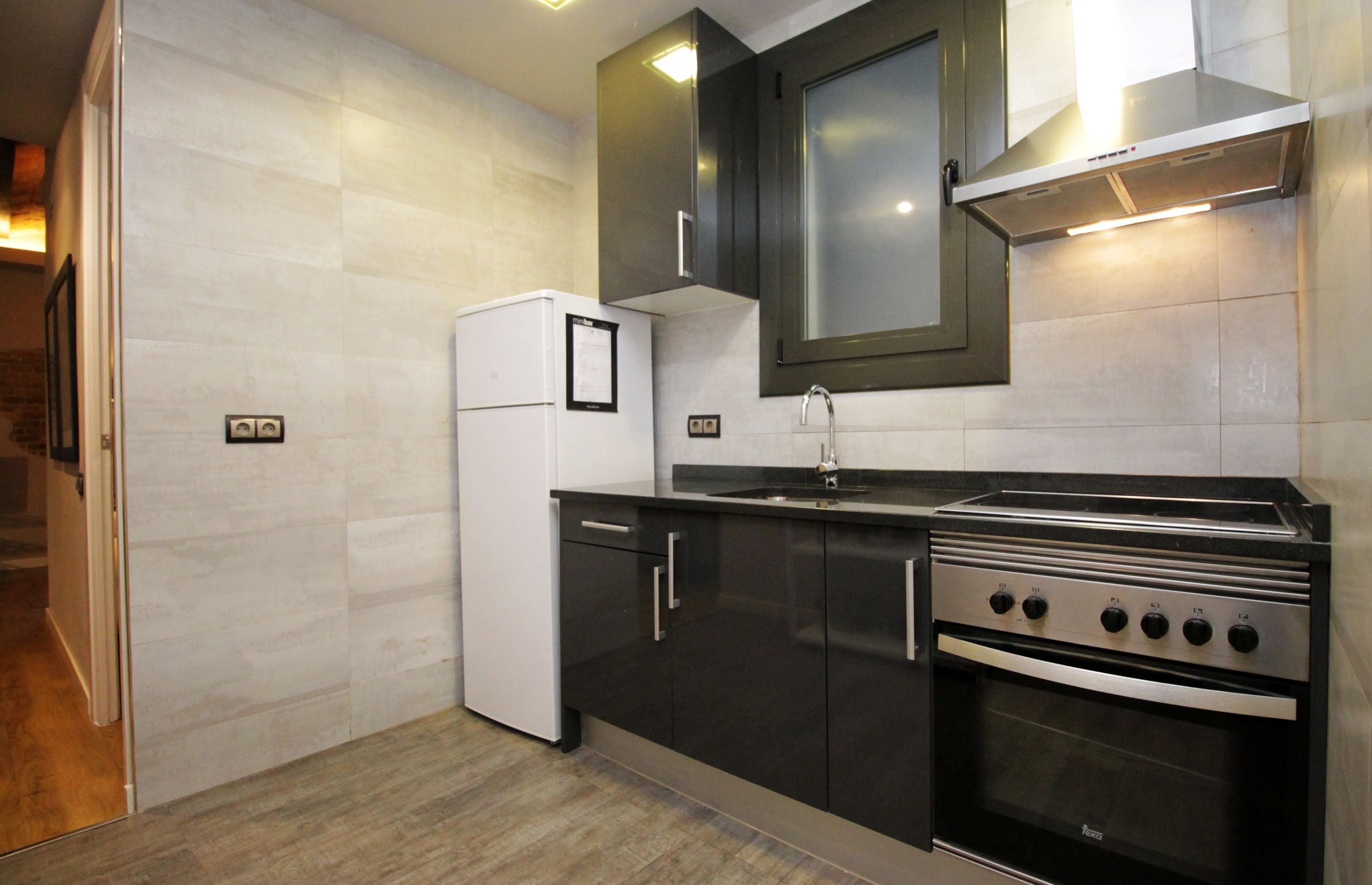 A modern kitchen with a built-in oven, a refrigerator, and dark cabinetry.