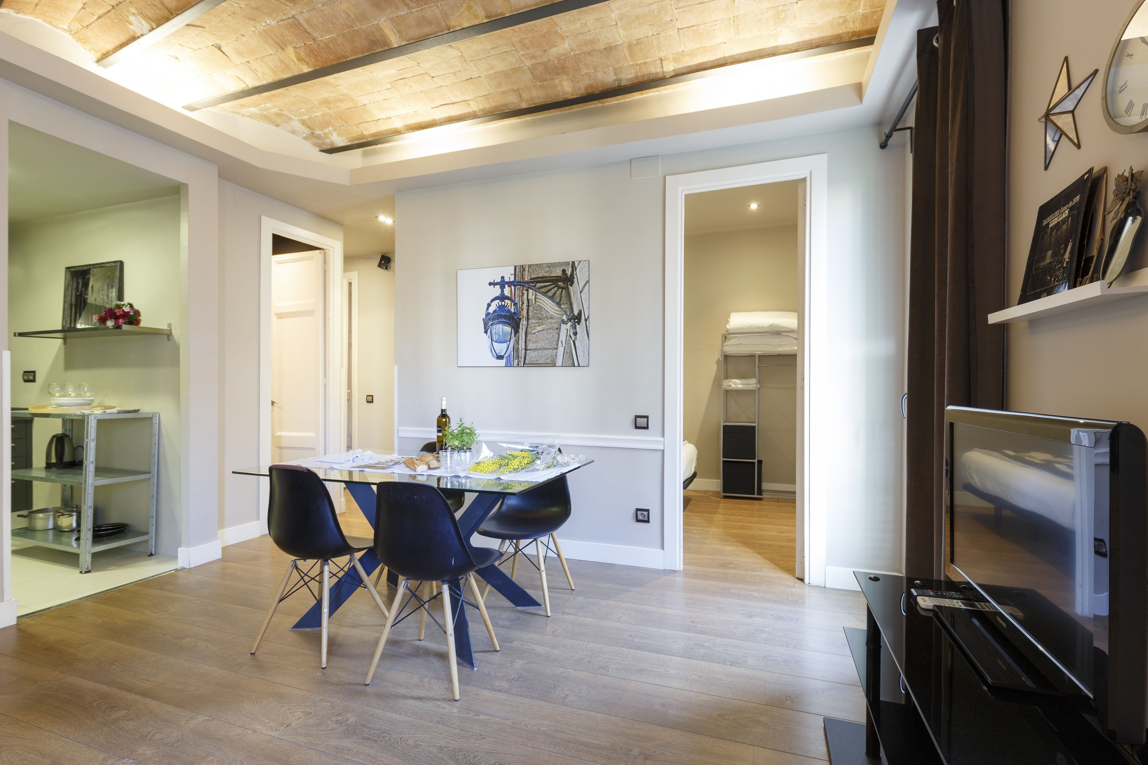A modern living room with a dining area, a TV, and a kitchen visible through an open door.