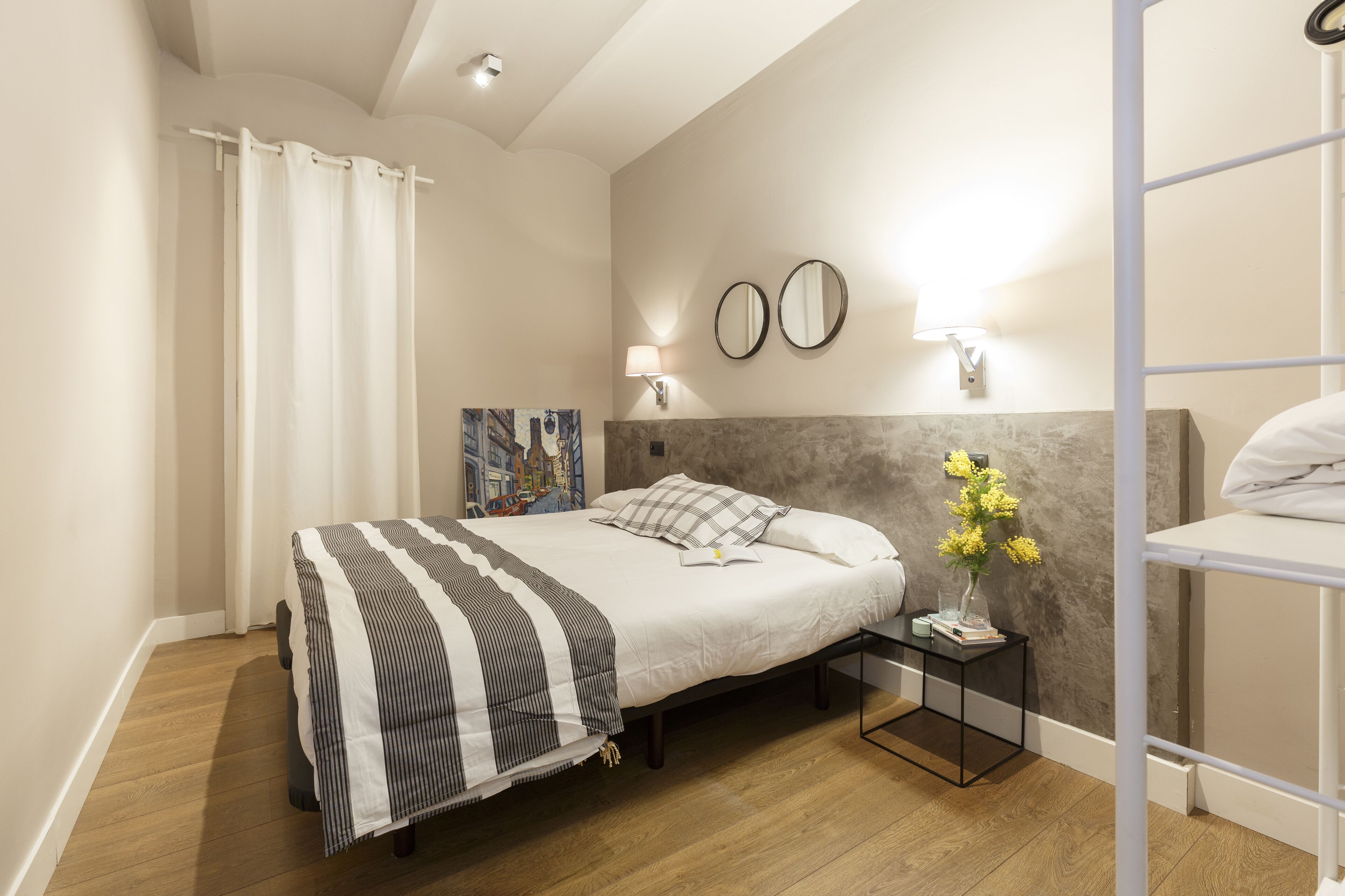 A neatly arranged bedroom with a bed, bedside tables, a nightstand, and a wall-mounted mirror.