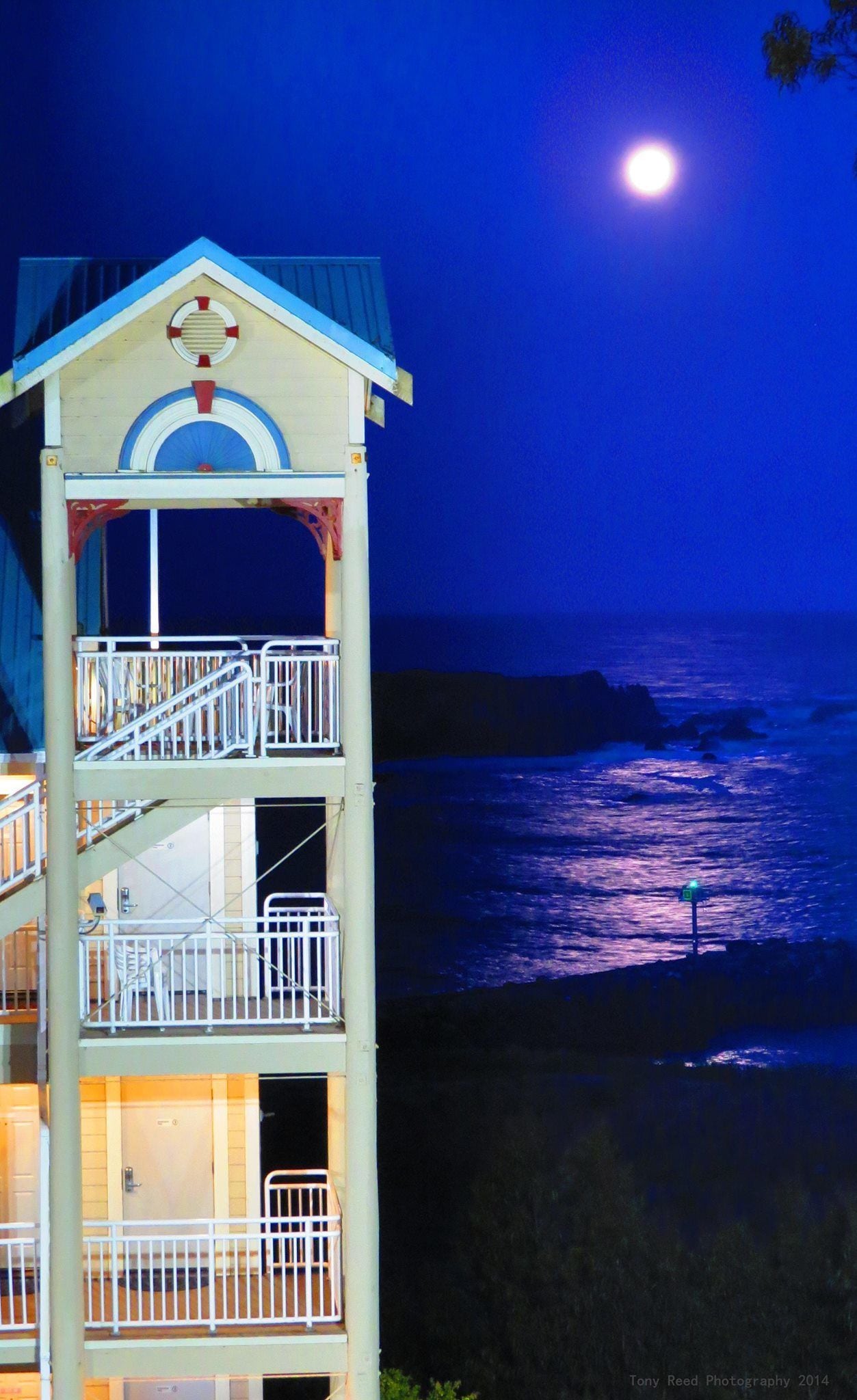 A multi-story building with balconies, a lifebuoy, and a view of the ocean at night.