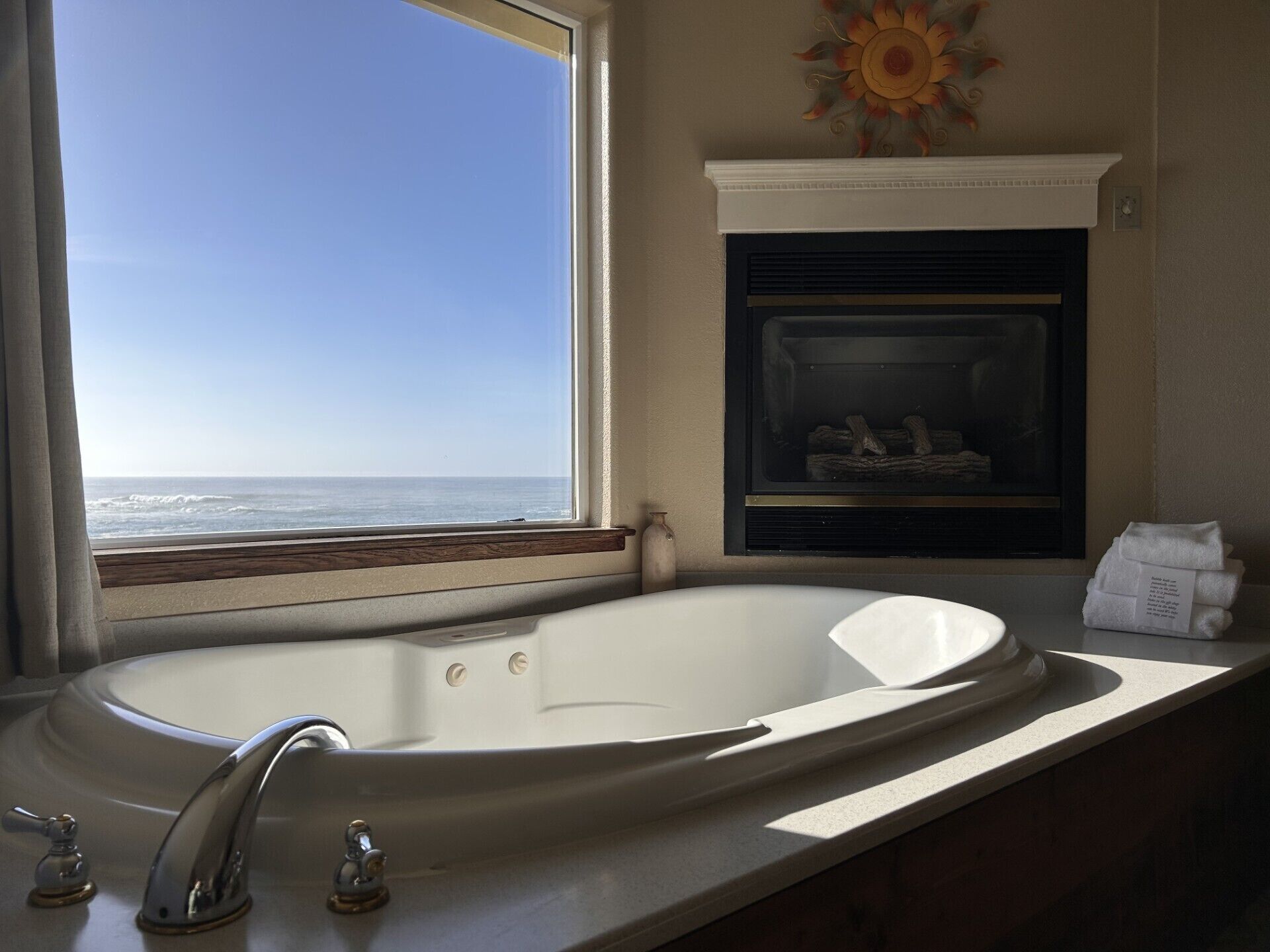 A bathroom with a large bathtub, a window with a view of the ocean, a fireplace, and a towel rack.