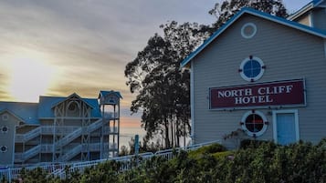 Experience the charm of the North Cliff Hotel, set amidst lush greenery with a traditional gabled roof and second-floor balcony.
