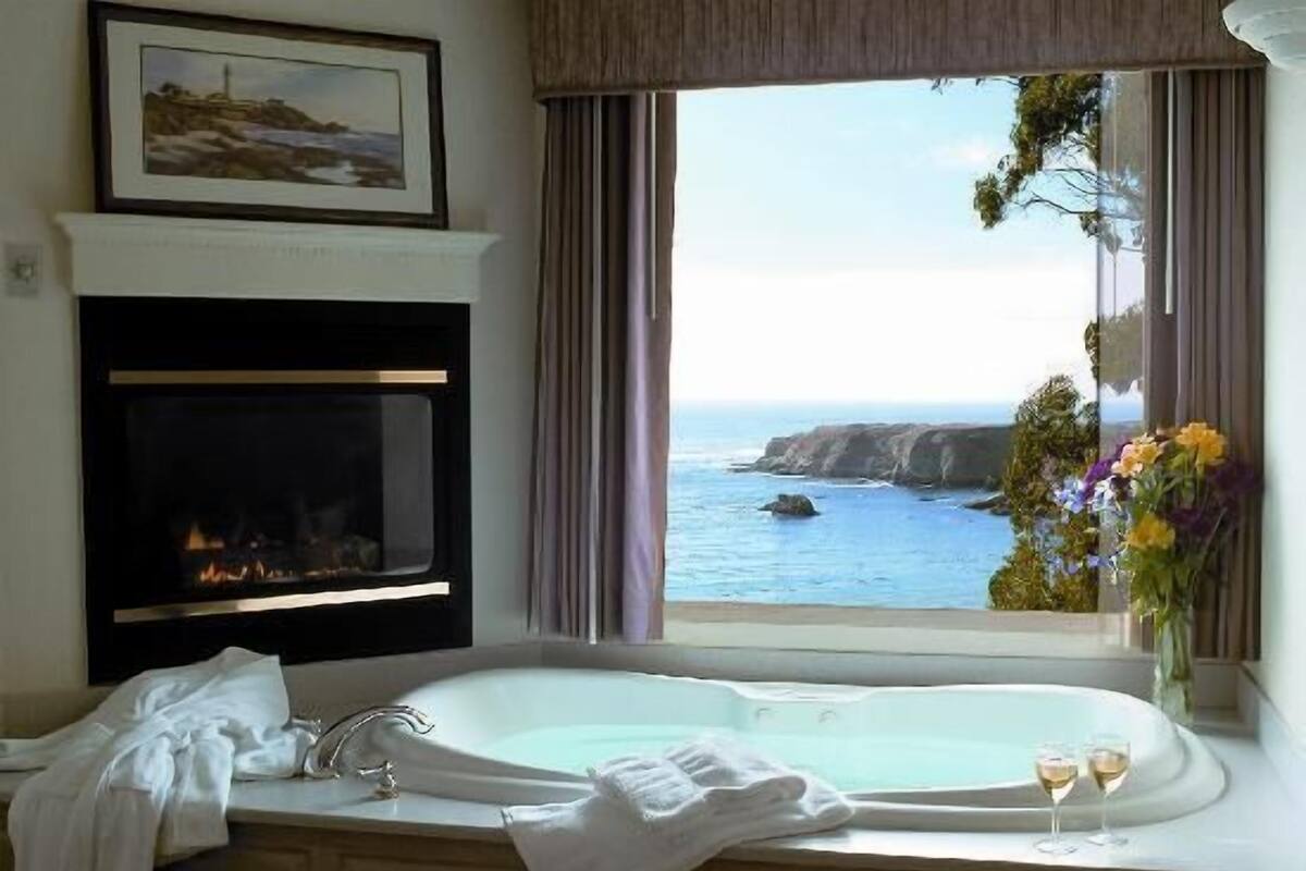 A bathroom with a large bathtub, a fireplace, and a view of the ocean.