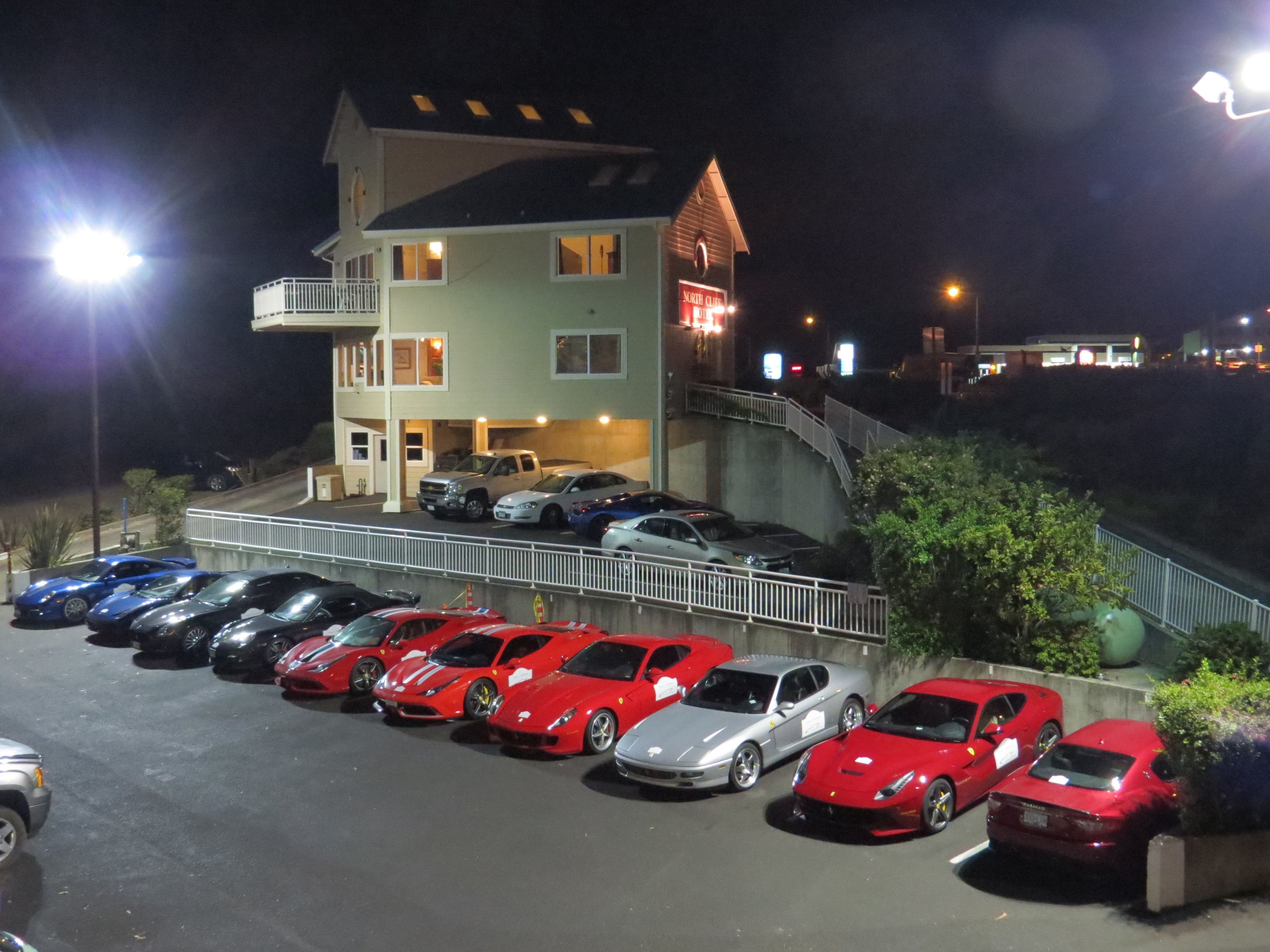 Un estacionamiento con varios coches de lujo, un edificio con balcón y una escalera que lleva al edificio.