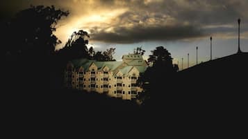 A multi-story building with a green roof, surrounded by trees and street lamps.