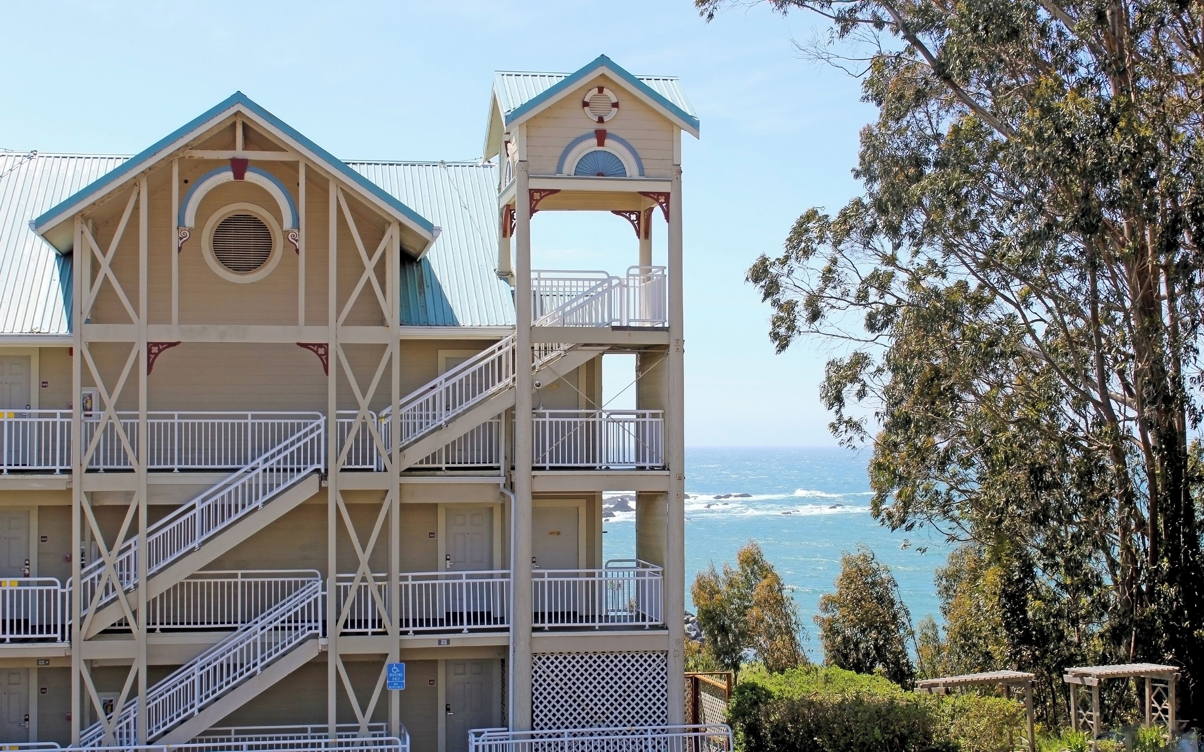 A multi-story building with a balcony on each floor, a lifebuoy on the roof, and a view of the ocean.