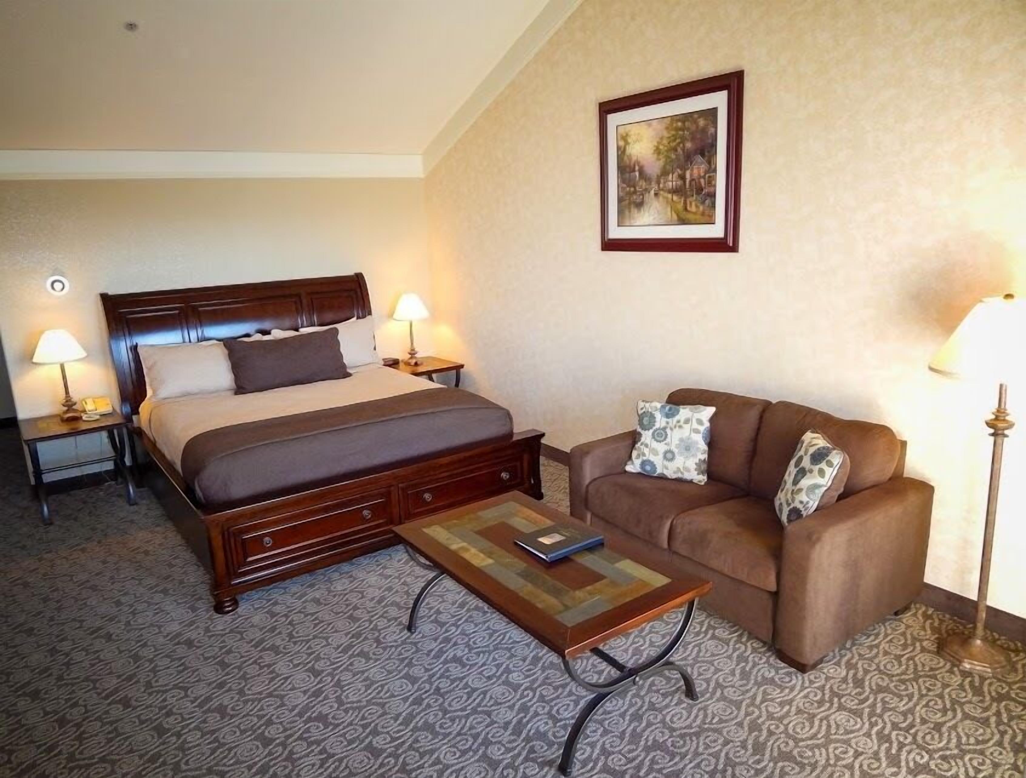 A hotel room with a bed, a sofa, a coffee table, and two bedside lamps.