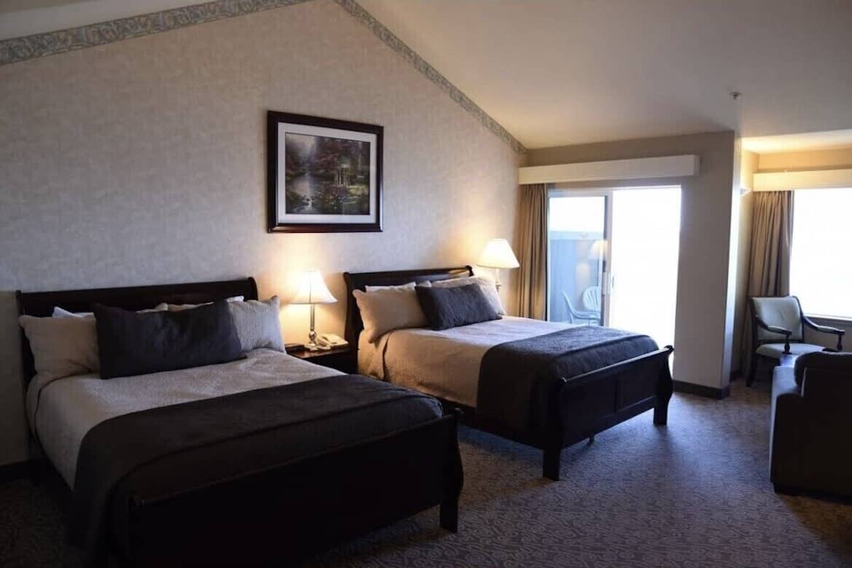 A hotel room with two beds, a desk, a chair, and a large window.