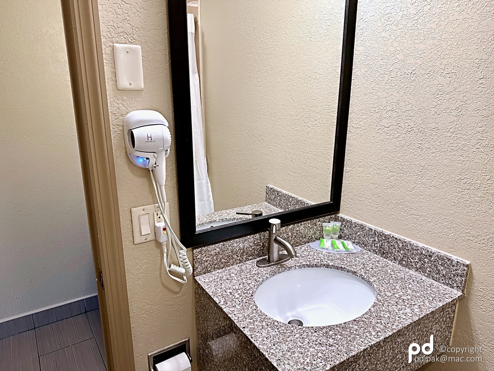 A bathroom with a granite sink, a mirror, a hairdryer, and a towel dispenser.