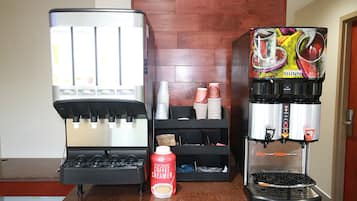 Una estación de café con dos máquinas de café, un dispensador de crema vegetal y vasos desechables apilados.