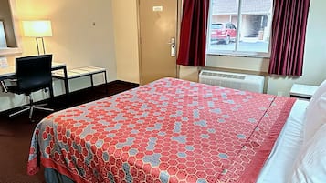 Habitación de hotel con cama, escritorio, silla, lámpara, ventana con cortinas y radiador.