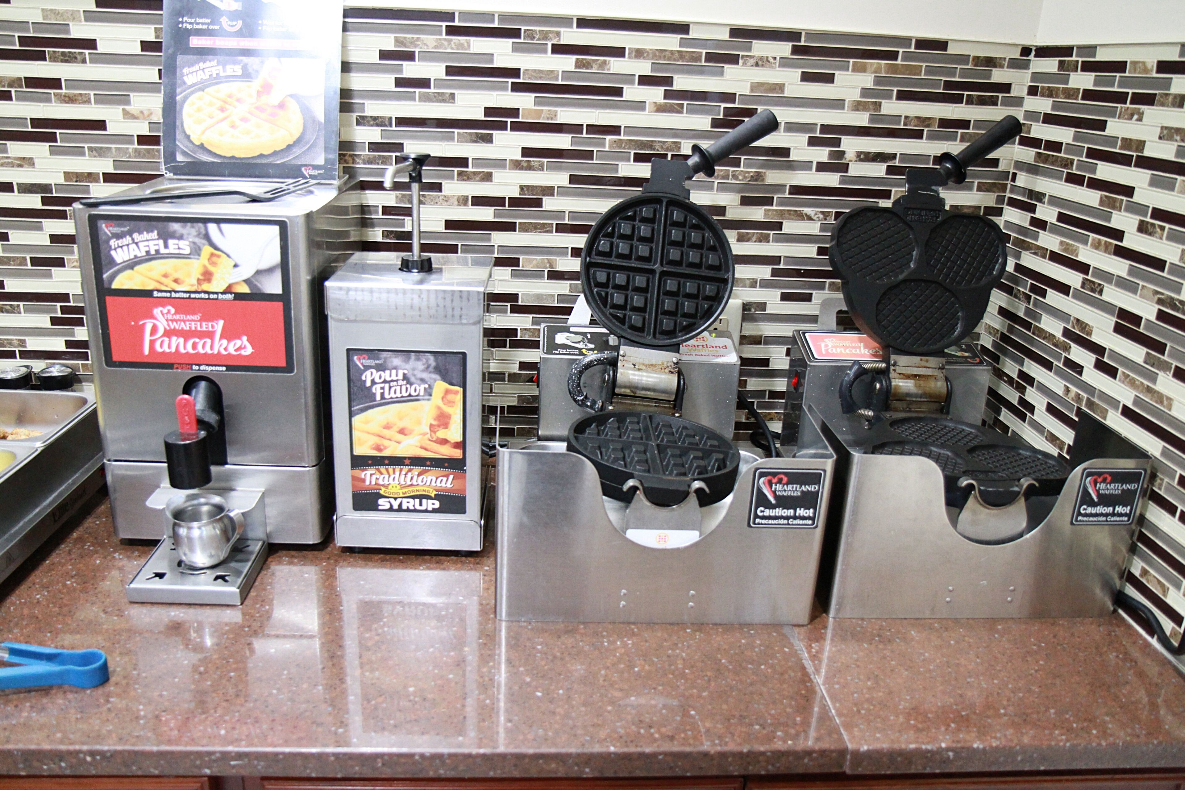 A waffle station with two waffle makers and a syrup dispenser.