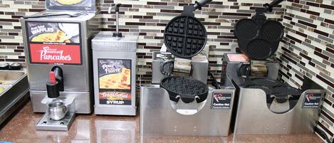 A waffle station with two waffle makers and a syrup dispenser.