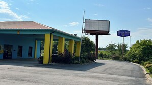 A building with a blue exterior and yellow pillars, a covered parking area, and a billboard advertising Motor Inns of America. - Motor Inns Of America (Madisonville)