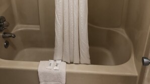 A bathtub with a white shower curtain, a towel, and toiletries on the side. - Motor Inns Of America (Madisonville)