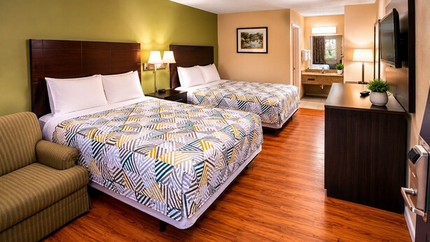 A hotel room with two beds, a sofa, a desk, a TV, and a bathroom visible in the background. - Motor Inns Of America (Madisonville)