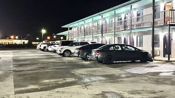 A motel with a row of parked cars, a covered parking area, and a building with multiple windows and doors.