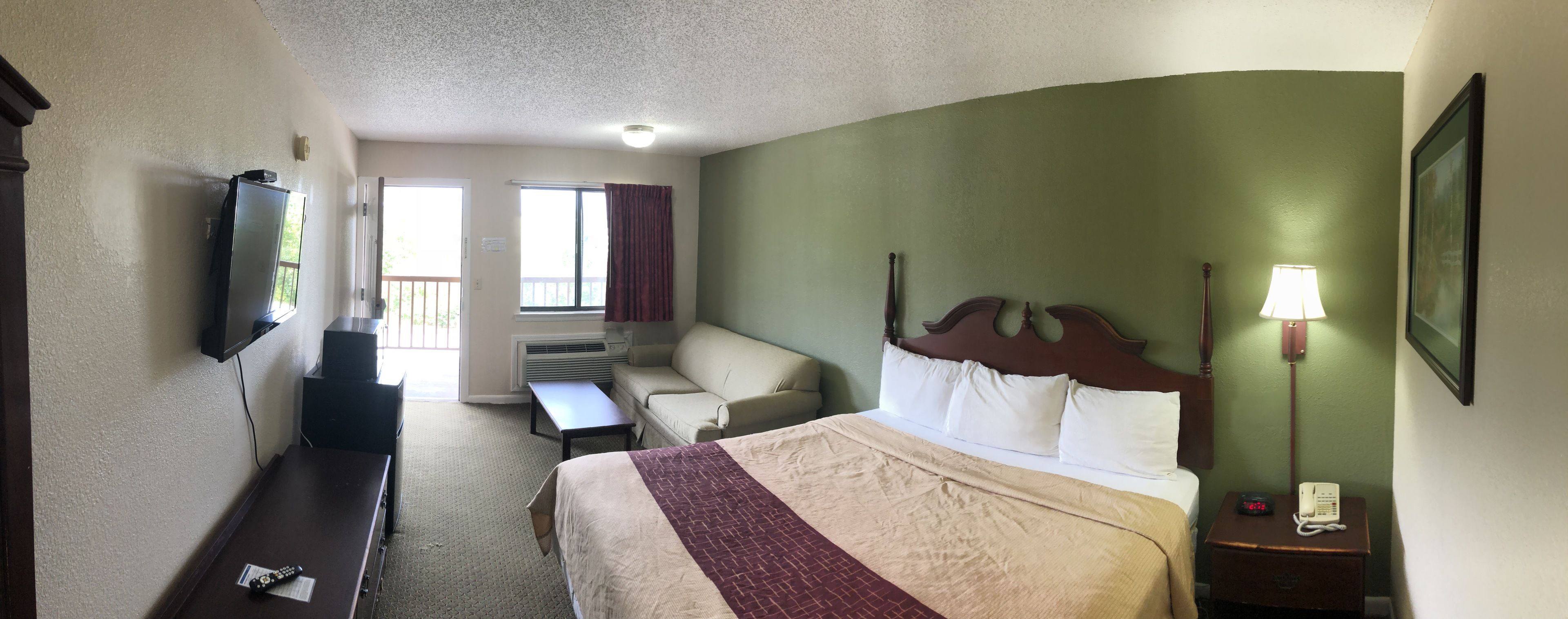 A hotel room with a bed, a desk, a television, a bench, and a window with curtains.