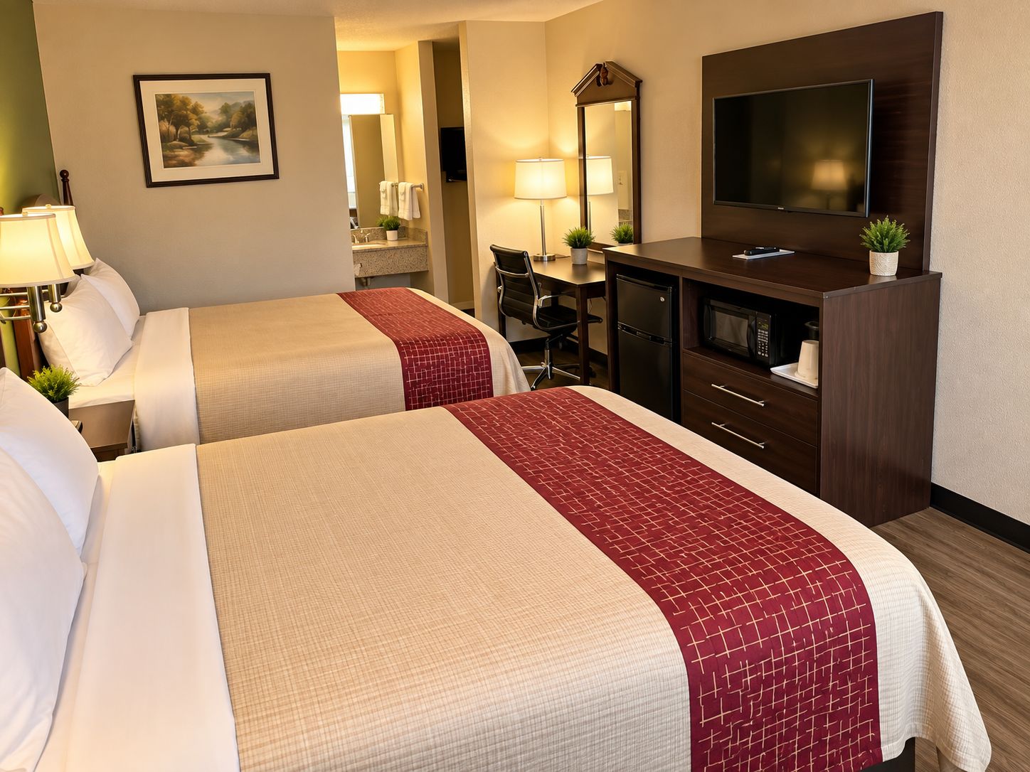 A hotel room with two beds, a desk, a television, and a bathroom visible in the background.