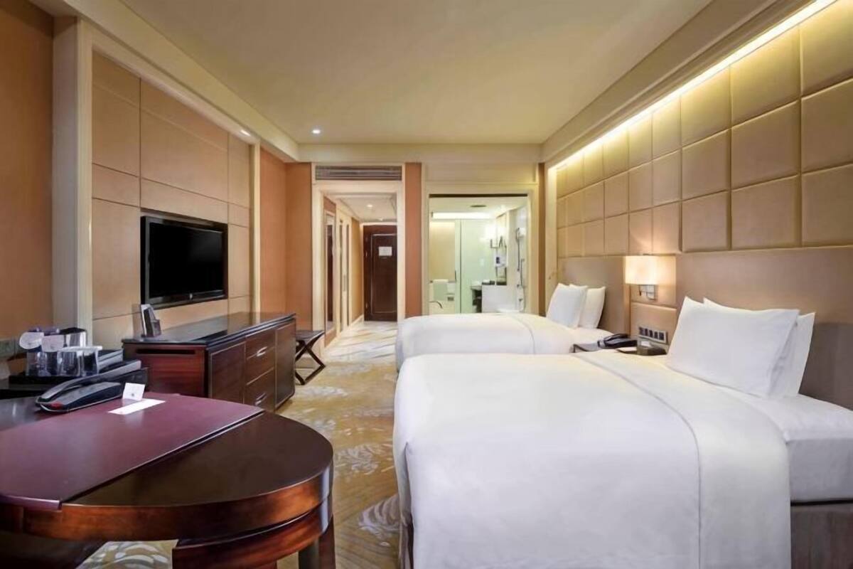 Habitación de hotel con dos camas, televisión, escritorio y baño a la vista.
