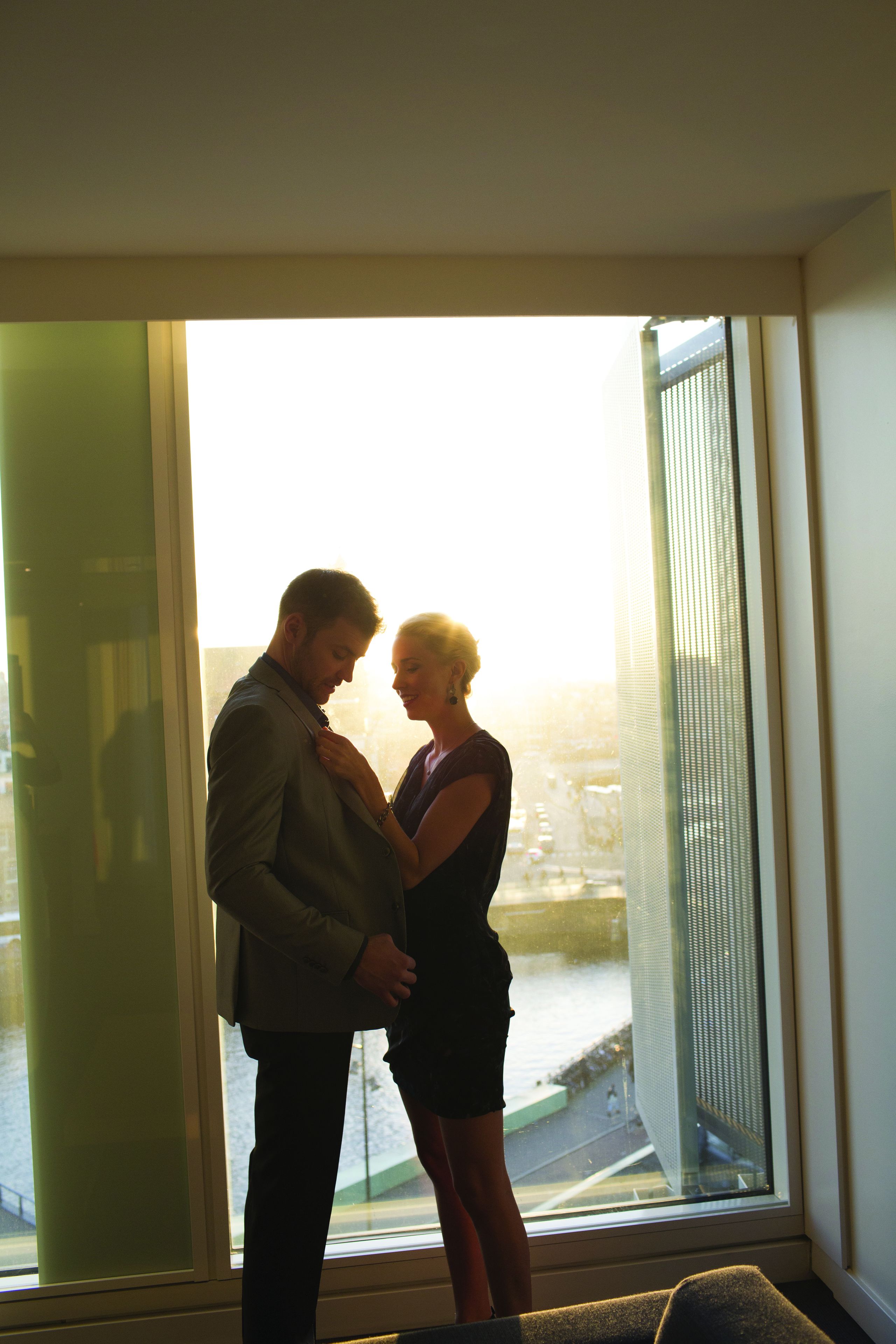 A couple standing by a large window with a view of a cityscape.