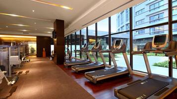 A gym with treadmills, weight machines, and large windows offering views of the outside.