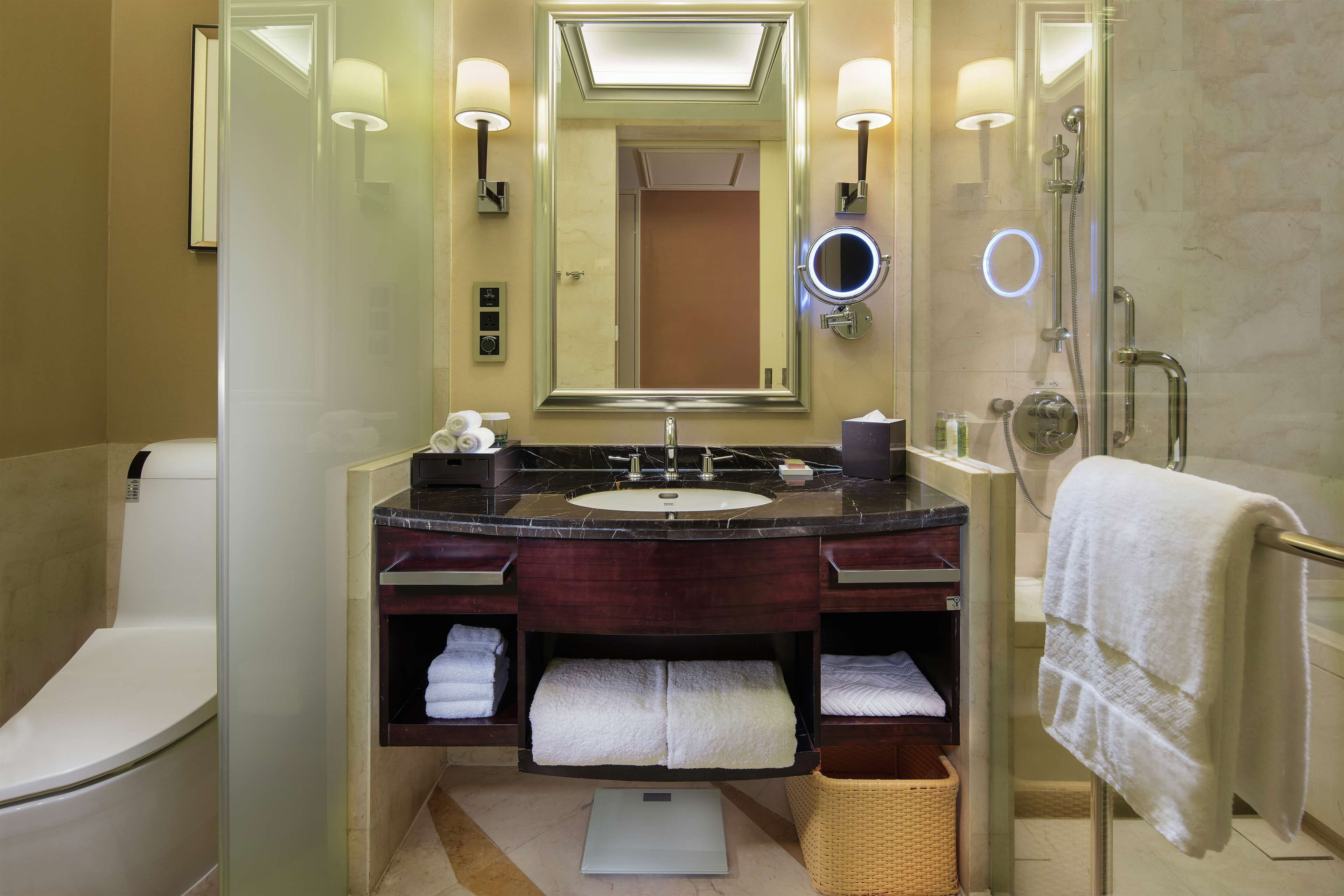 Une salle de bain moderne avec un grand miroir, un lavabo et une douche. On peut voir des serviettes et des articles de toilette.
