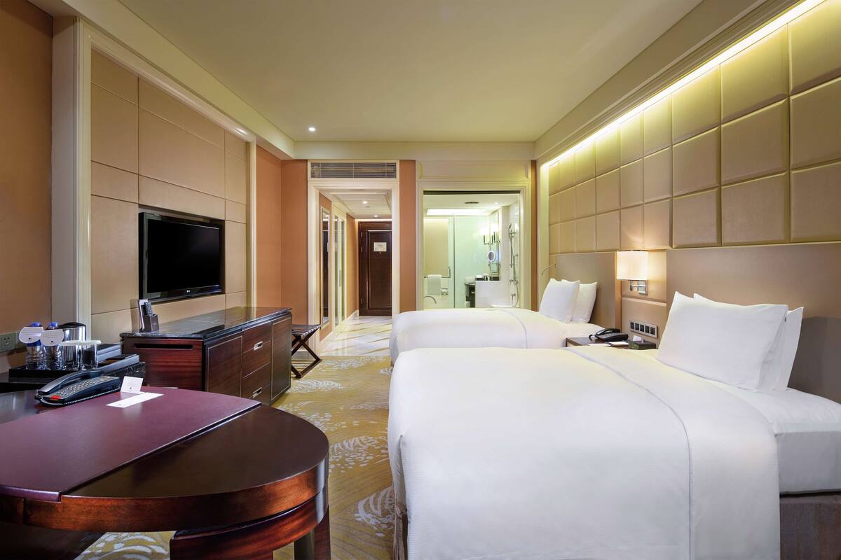 Habitación de hotel con dos camas, un escritorio con teléfono, un televisor de pantalla plana y un minibar.