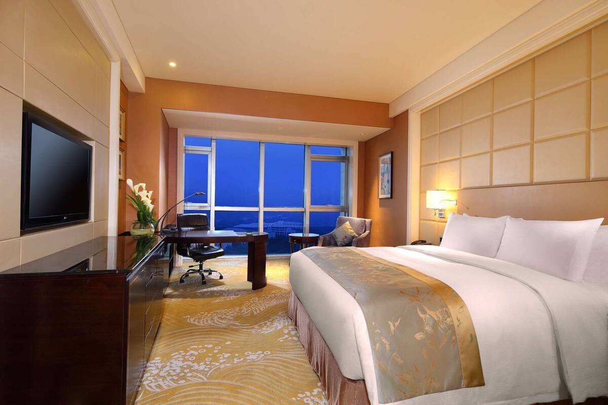 Habitación de hotel con una cama grande, un escritorio, una silla, un televisor y vista al océano.