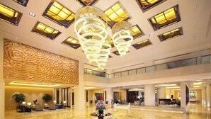 Eine großzügige Lobby mit einer zentralen Blumenkomposition, einer hohen Decke mit modernen Kronleuchtern und einem polierten Marmorboden.