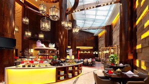 Eine großzügige Hotelhalle mit einer zentralen Bar, hohen Decken und modernen Lichtelementen.