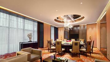 A hotel room with a dining area, large windows, and a chandelier.