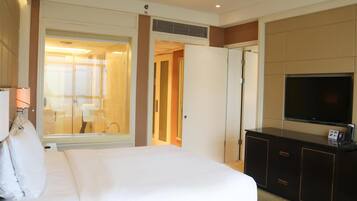 Habitación de hotel con cama, televisor, minibar y baño visible a través de una puerta abierta.