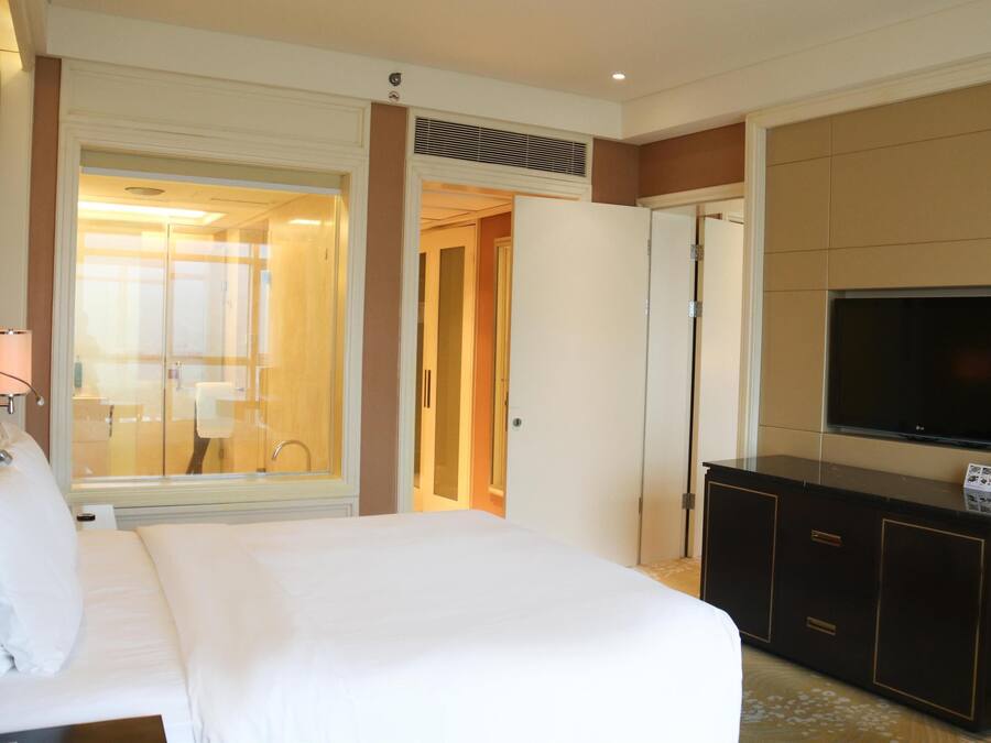 Habitación de hotel con cama, televisor, minibar y baño visible a través de una puerta abierta.