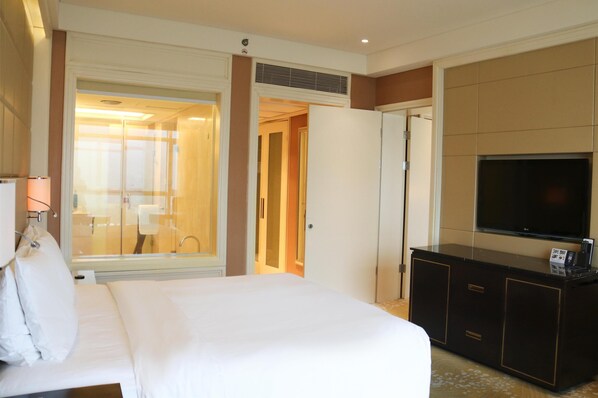A hotel room with a bed, a TV, a minibar, and a bathroom visible through an open door.