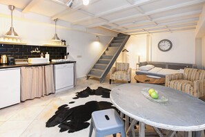 Une cuisine moderne avec un tapis en peau de vache noir et blanc, une table à manger ornée de pommes et un escalier menant à une chambre à coucher située en mezzanine.