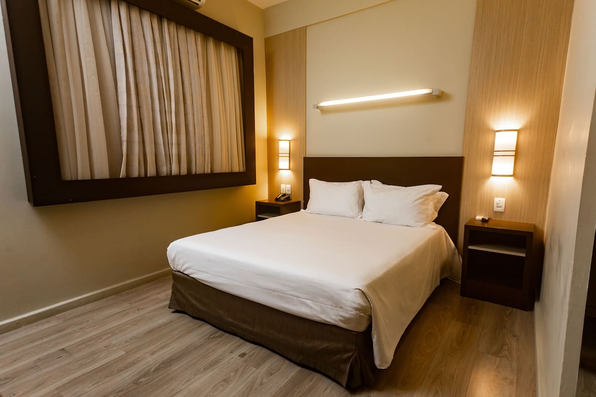 Ein Hotelzimmer mit einem großen Bett, zwei Nachttischen, einer Wandleuchte und einem Vorhang.