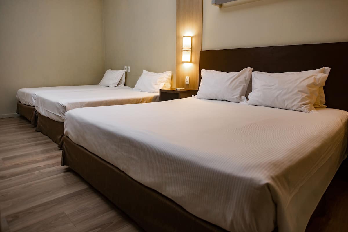 Ein Hotelzimmer mit zwei Einzelbetten und einem größeren Bett, alle mit weißer Bettwäsche.