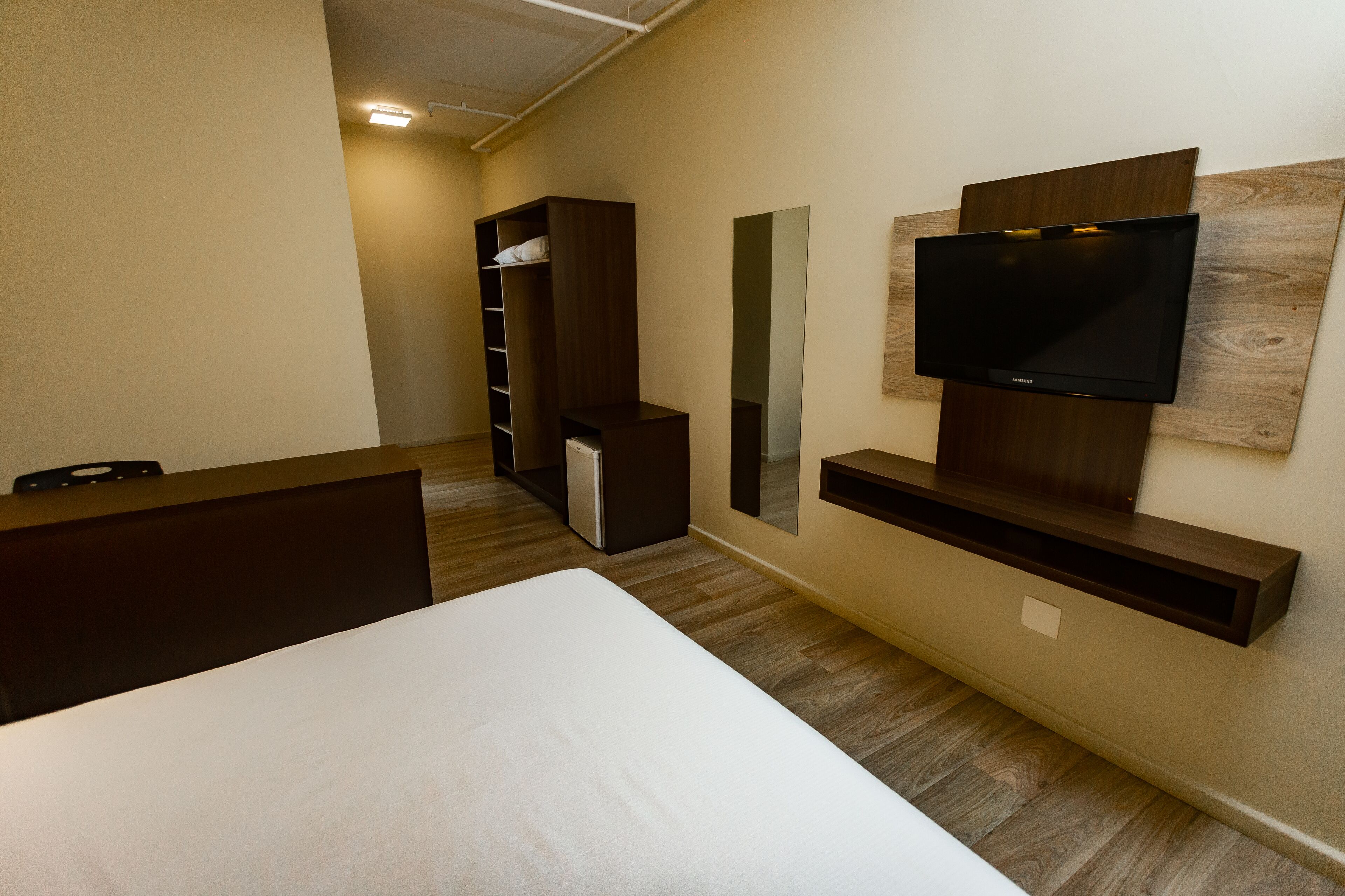 A hotel room with a bed, a TV mounted on the wall, a wardrobe, and a mirror.