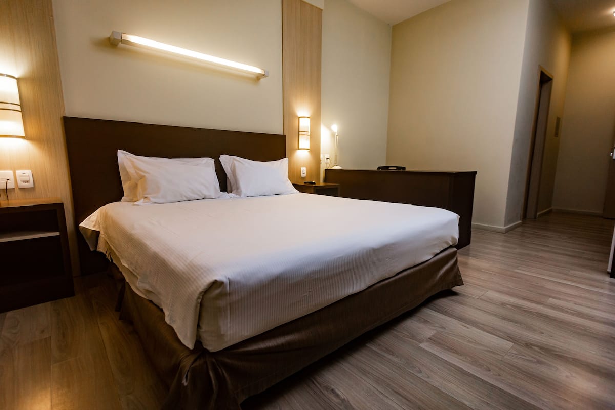 Ein Hotelzimmer mit einem großen Bett, Holzboden, einem Nachttisch mit Lampe und einer Wandleuchte.