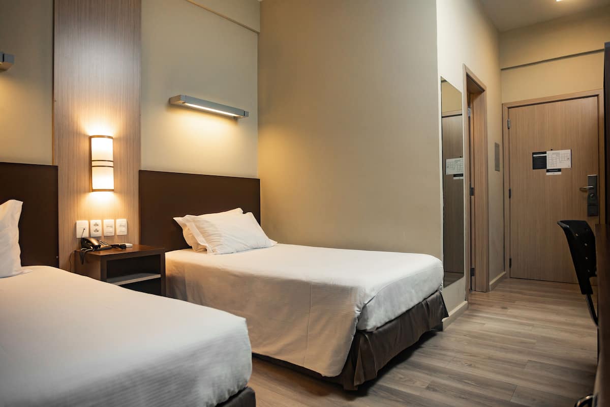 Ein Hotelzimmer mit zwei Betten, einem Schreibtisch mit Lampe und einer Tür mit einem Schild.
