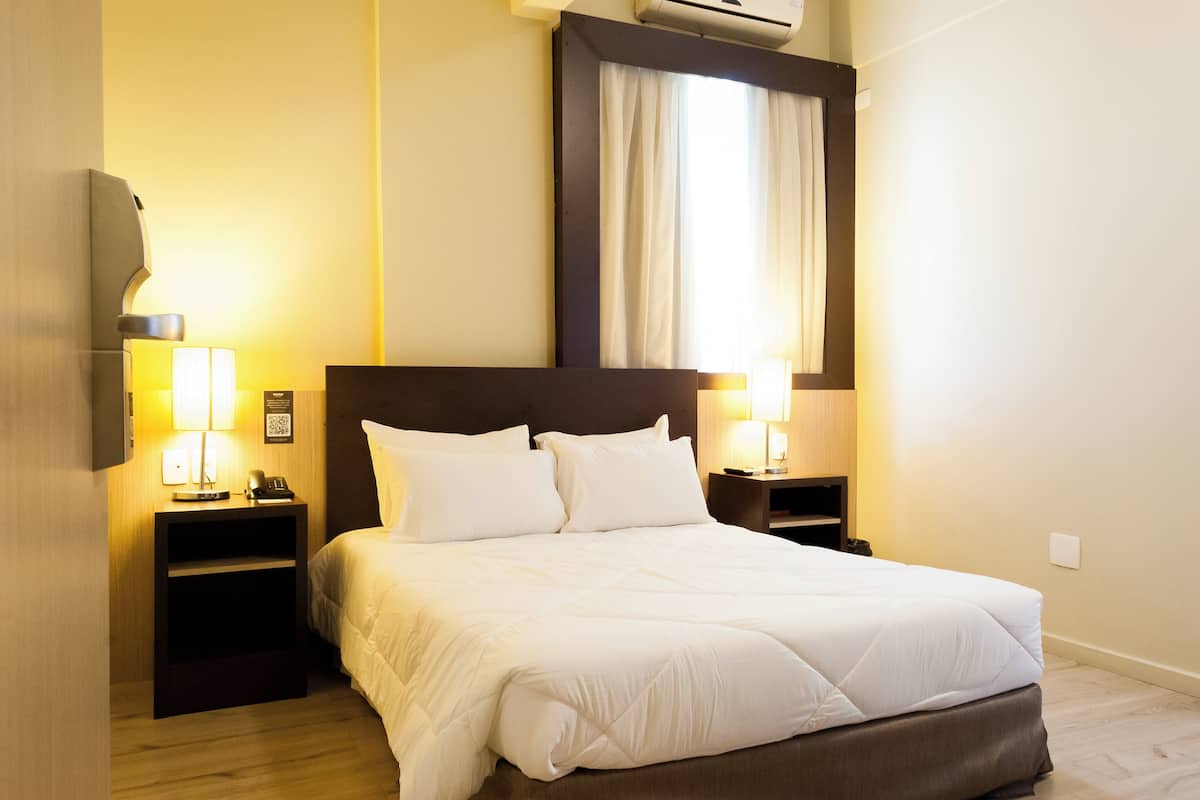 Ein Hotelzimmer mit einem großen Bett, zwei Nachttischen mit Lampen, einem Flachbildfernseher und einer Klimaanlage.