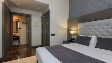 A hotel room with a large bed, a bedside table with a lamp, a wardrobe, and a bathroom visible through an open door.