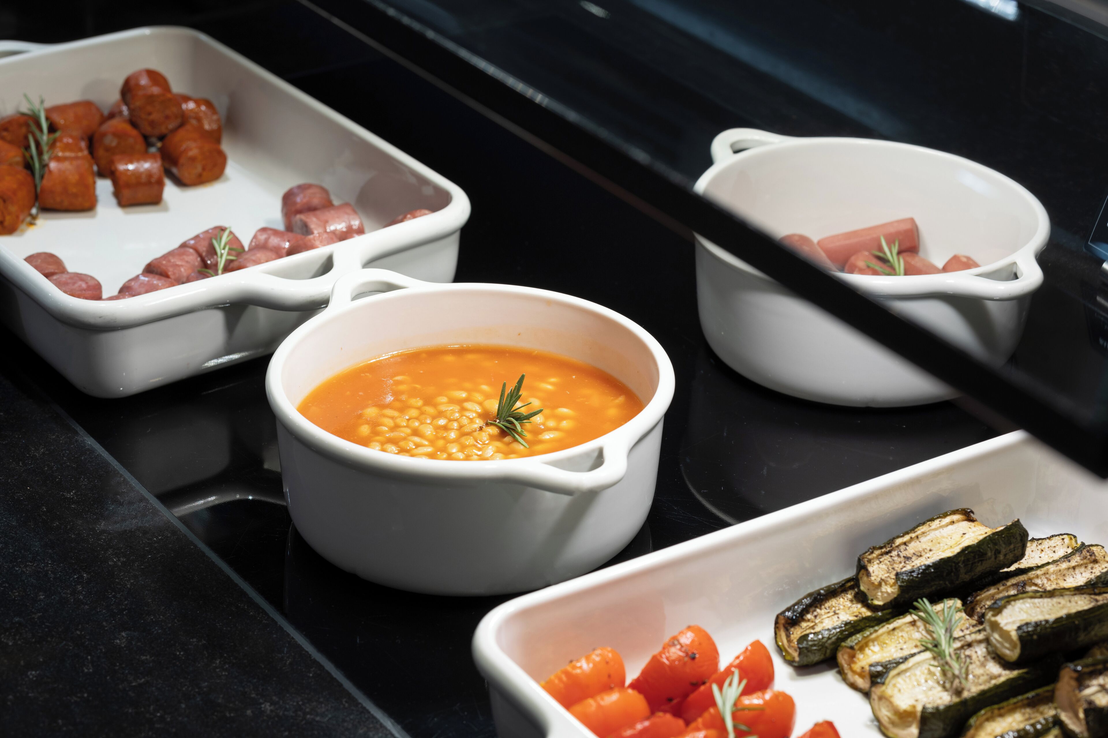 A buffet with various dishes including sausages, beans, and roasted vegetables.