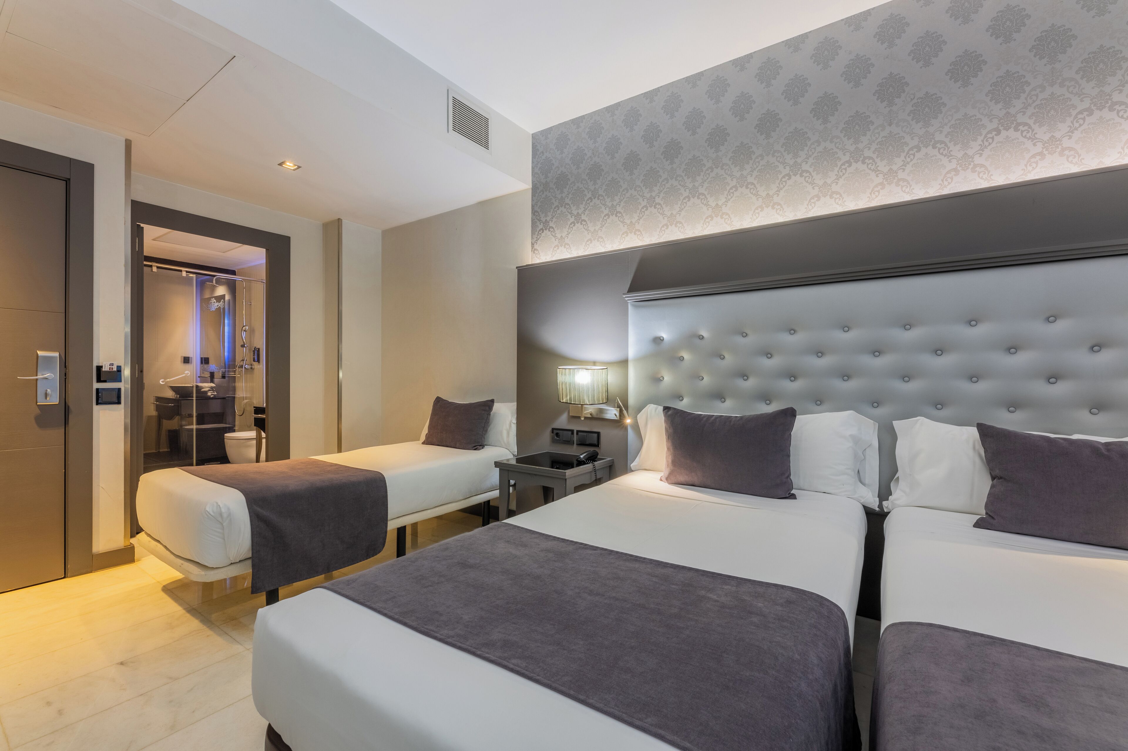 Habitación de hotel con dos camas, baño y zona de ducha.