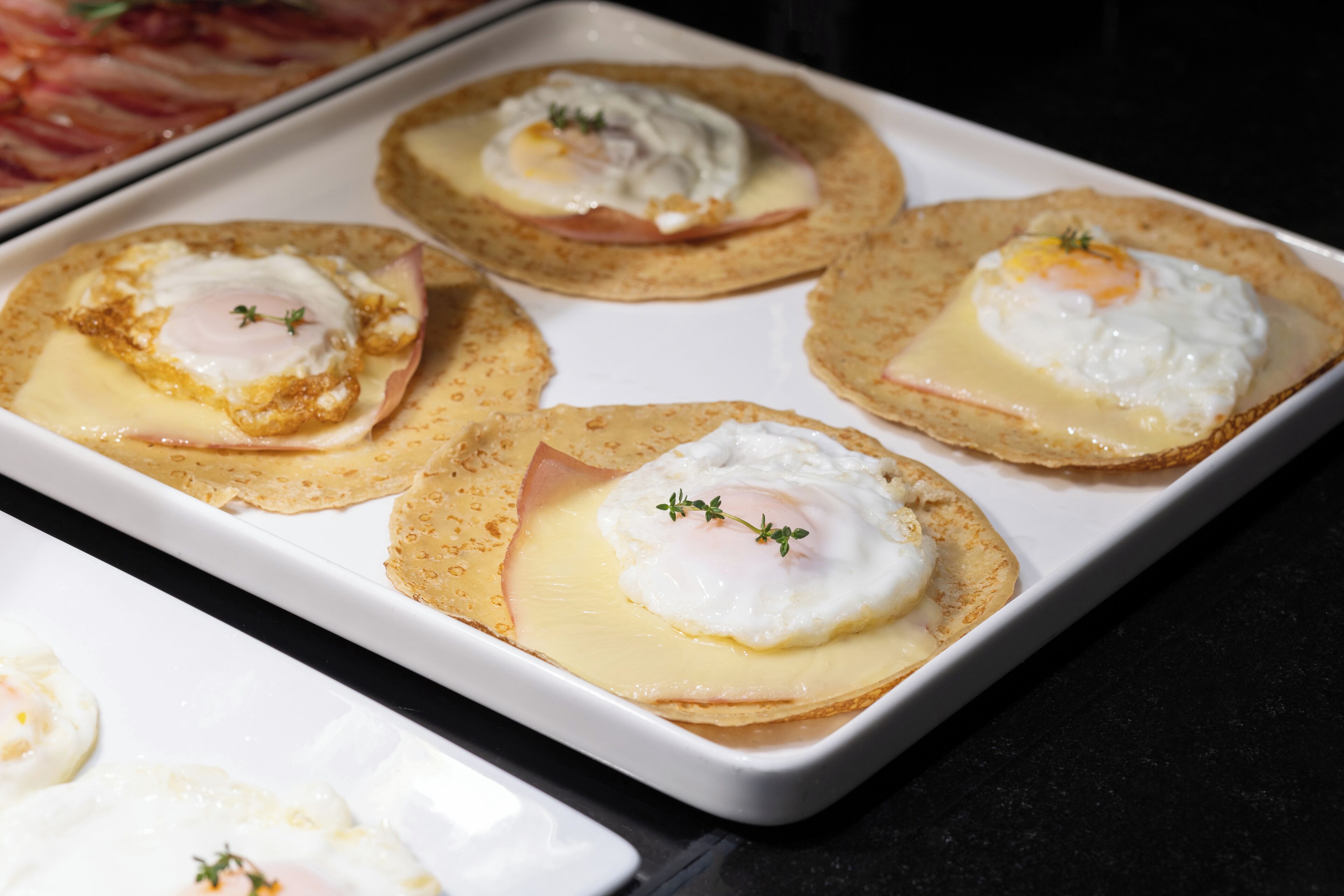 Una bandeja con huevos Benedictos, jamón y salsa holandesa sobre tostadas.